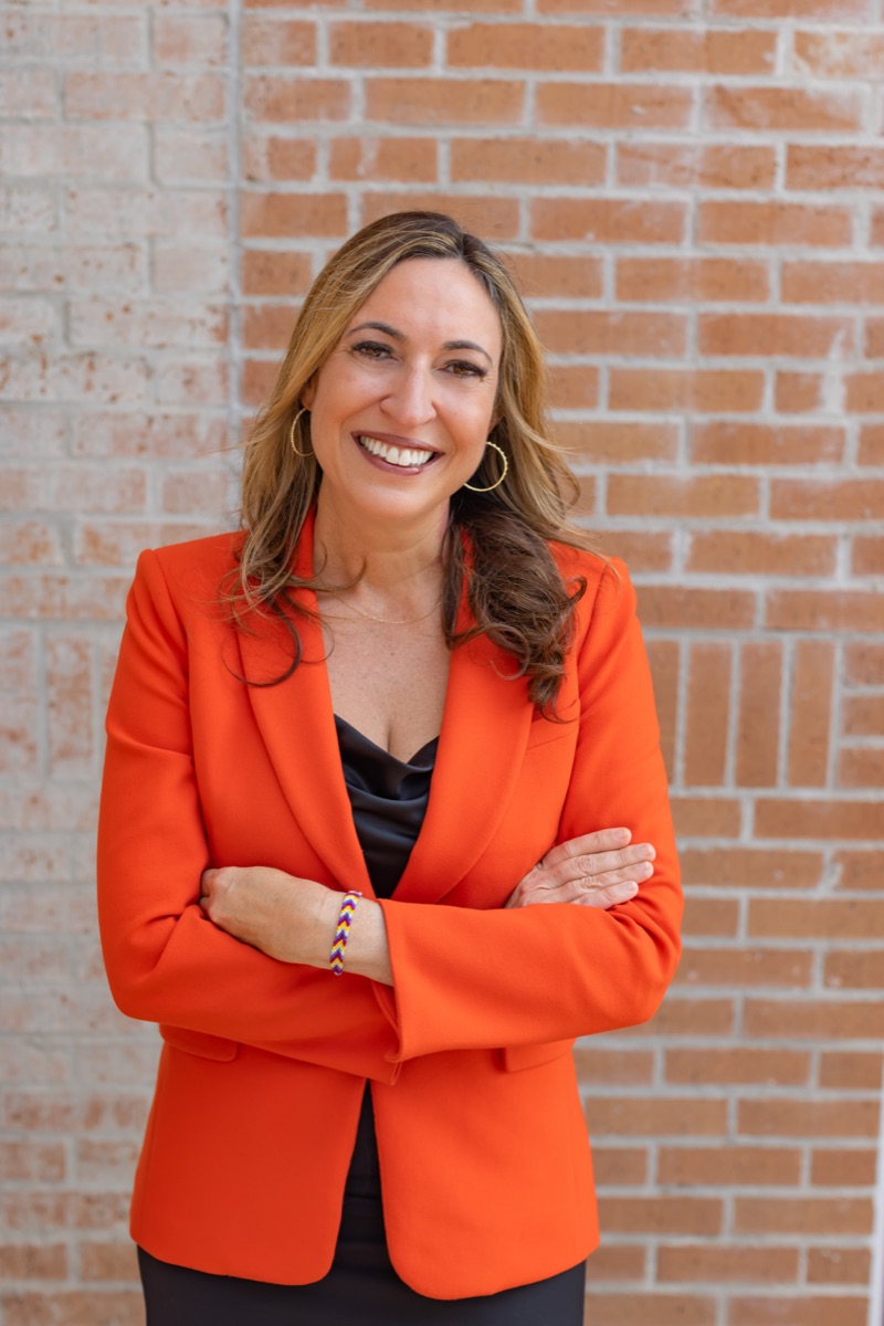 Dr. Emily Triana Marx smiling, arms crossed, wearing an orange blazer